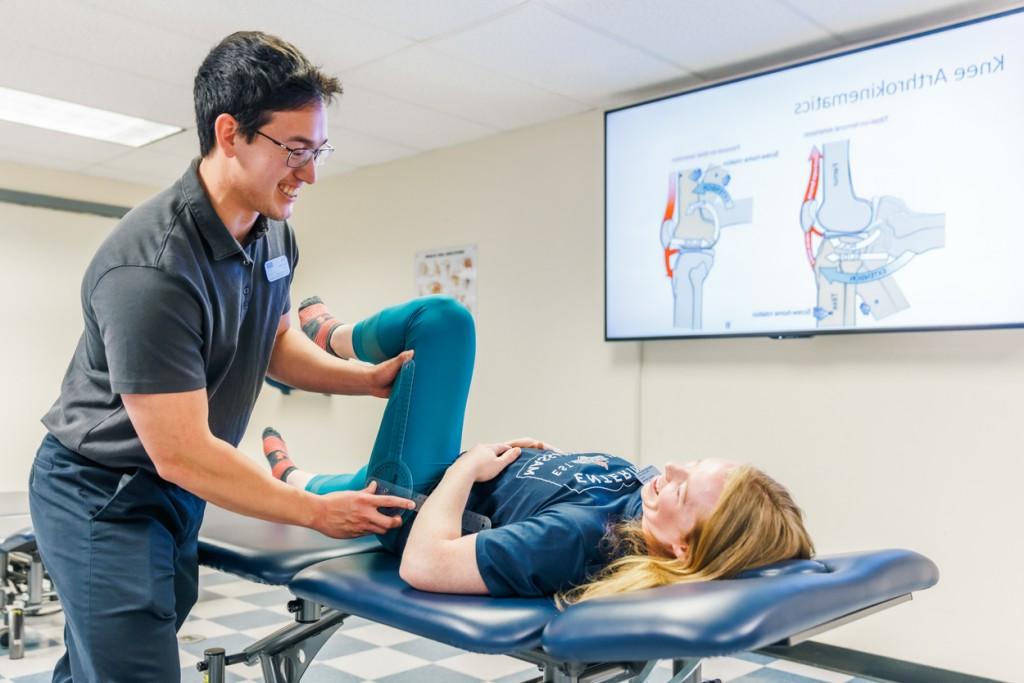 A physical therapy student practices checking a patient's leg mobility
